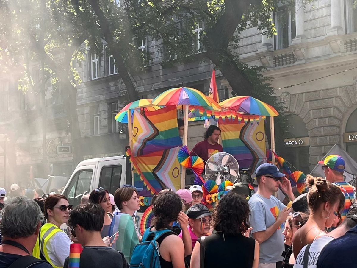 Crowds at the Budapest Pride march walking behind a float decorated in rainbow colours