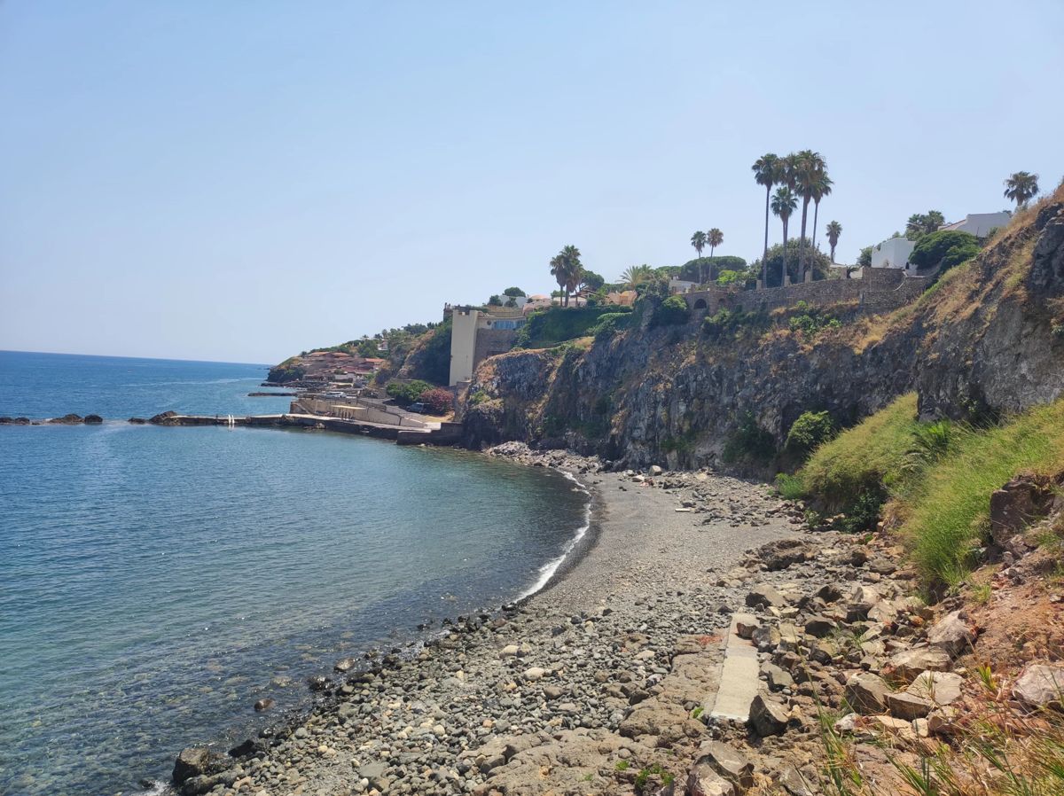 A quiet pebble beach and reef on the eastern coast of Sicily under a clear blue sky
