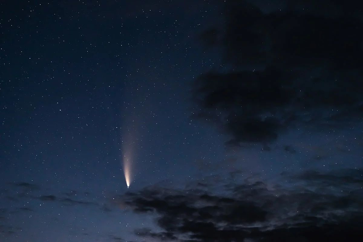 A meteor streaking across a deep blue night sky above dark clouds